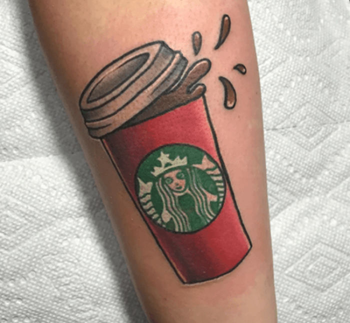 A vibrant tattoo of a Starbucks coffee cup on an arm, with splash details.