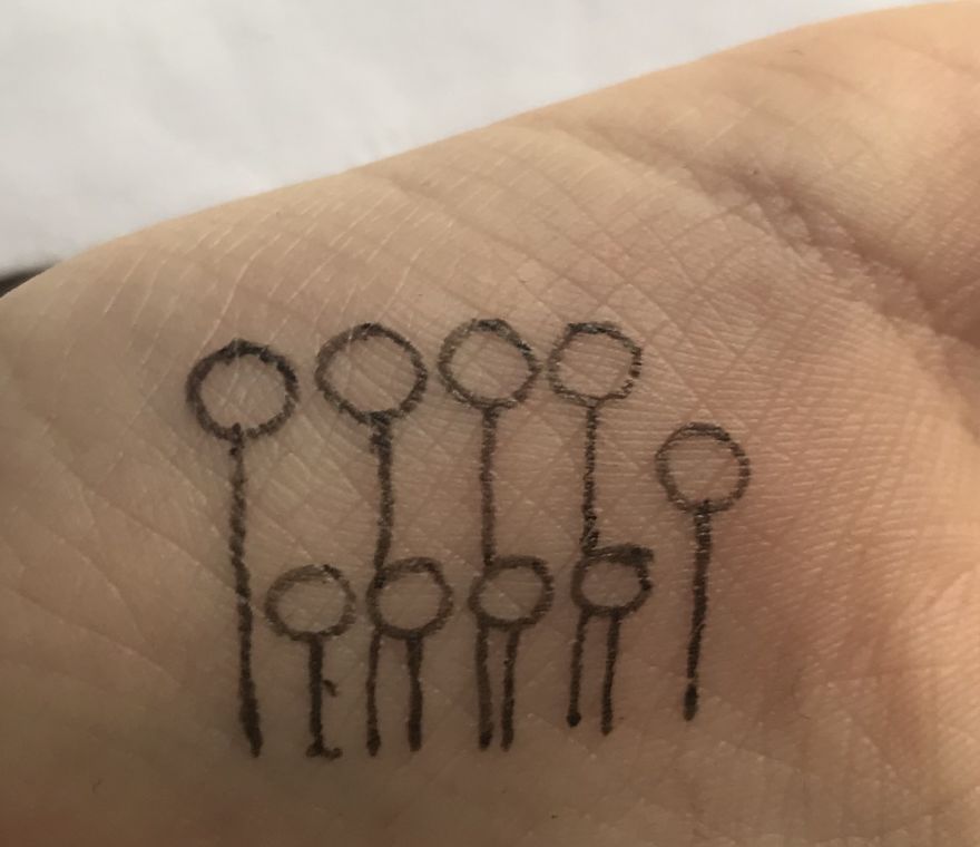 Hand-drawn J. R. R. Tolkien inspired tattoo sketch on palm with simple circular and line designs.