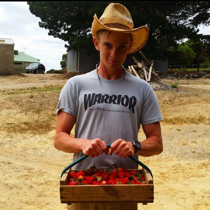 Young man wearing a cowboy hat holding a crate of fresh strawberries, representing vegan hunters outdoors.