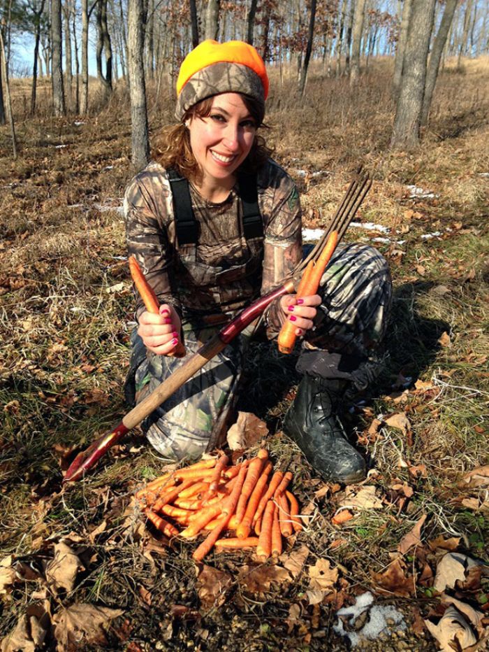 Smiling woman in camouflage gear harvesting fresh carrots in the forest, a funny vegan hunter with a garden fork.