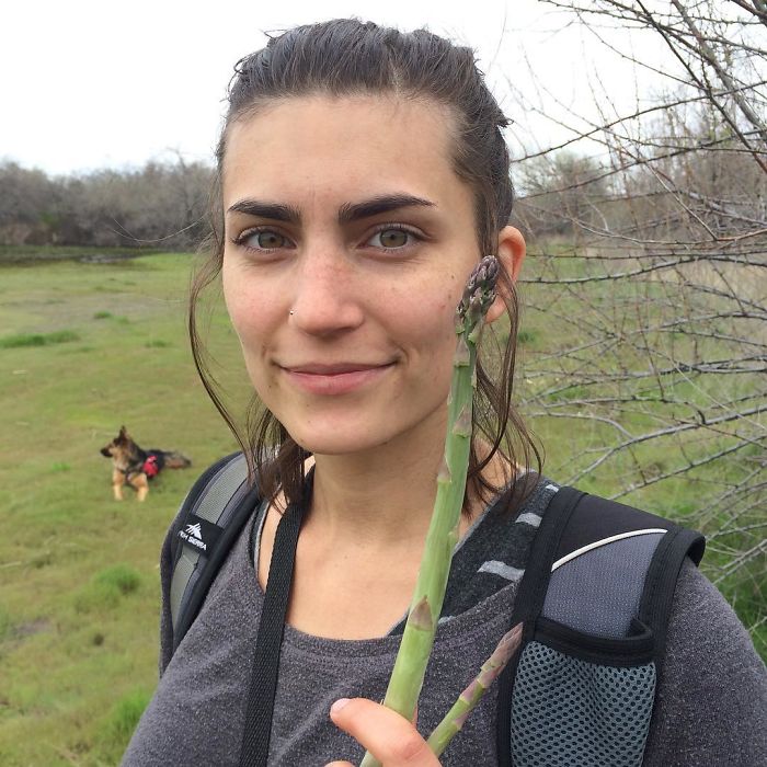 Young woman outdoors holding fresh asparagus stalk, illustrating funny pics of vegan hunters in a natural setting.