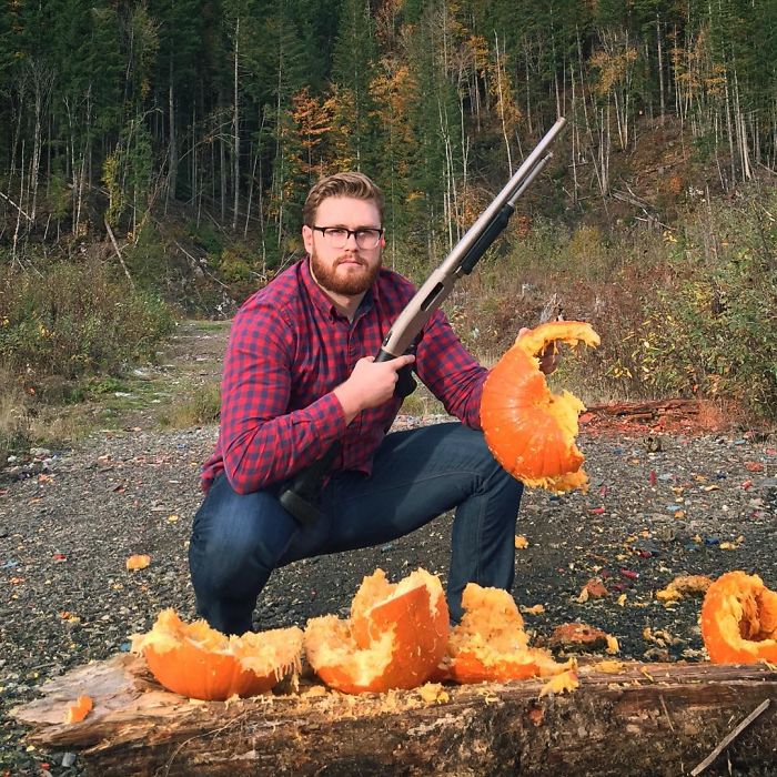 Man dressed in plaid holding a s*****n and a broken pumpkin in a forest clearing, funny vegan hunters concept.