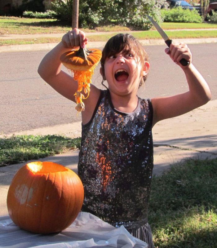 Child holding pumpkin guts with knife and fork outdoors, a funny vegan hunter moment with pumpkin as the main focus.
