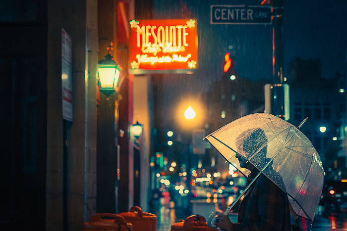 Person holding transparent umbrella on rainy night in one of the most dangerous cities in America with neon lights and wet street.