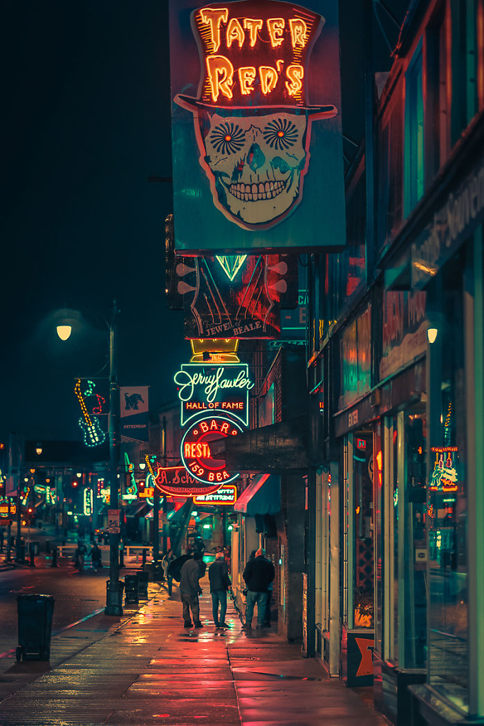 Night street scene in one of the most dangerous cities in America with neon bar signs and people walking on wet sidewalk.