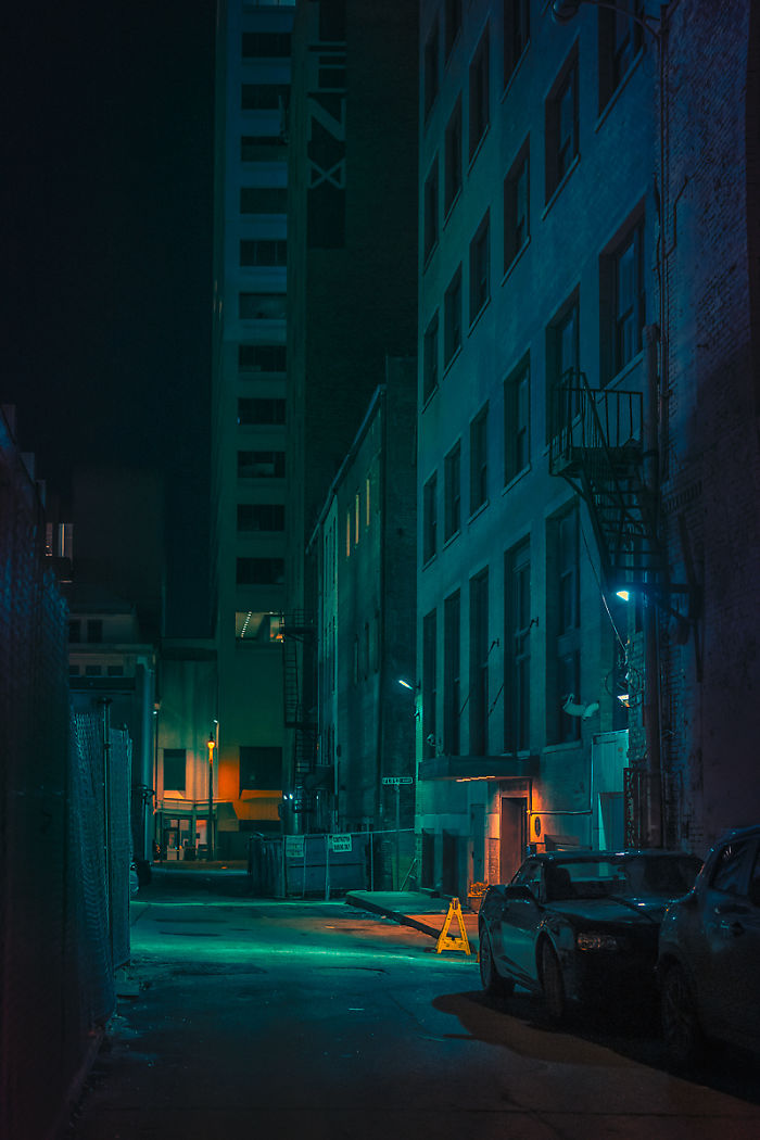Dark urban alley at night in one of the most dangerous cities in America with parked cars and dim street lighting.