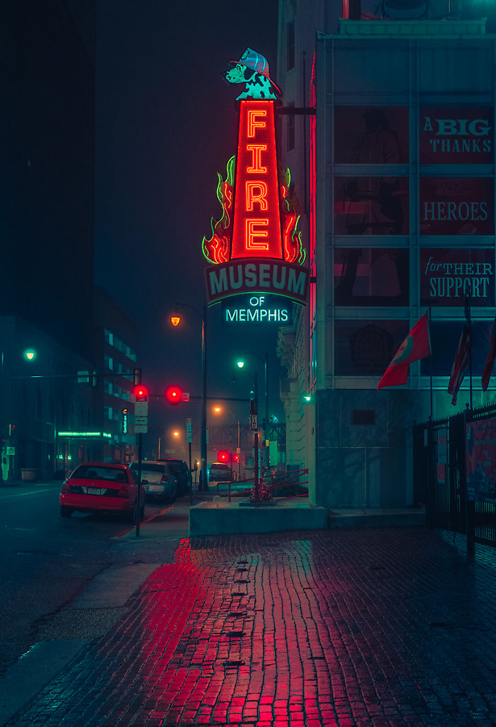 Neon Fire Museum of Memphis sign glowing at night on city street reflecting on wet brick sidewalk.