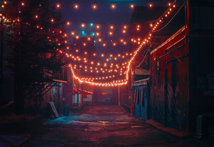Dimly lit urban alley in one of the most dangerous cities in America, with string lights overhead and worn buildings.