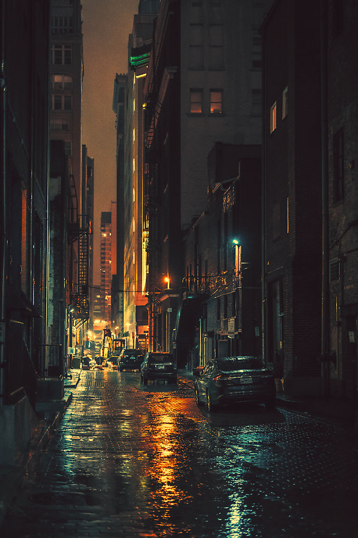 Dimly lit urban alley at night with wet reflective streets and parked cars in one of the most dangerous cities in America.