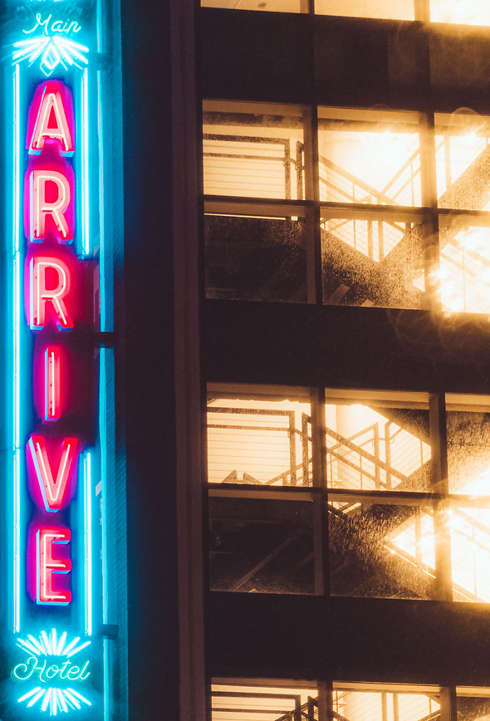 Neon sign for a drive-in hotel glowing at night with illuminated staircases inside a city building.
