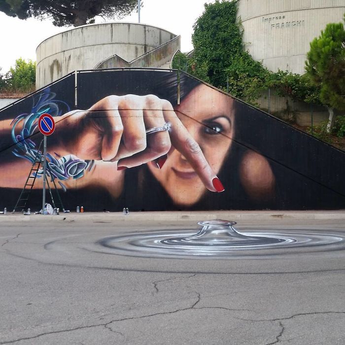 3D street art of a woman’s hand interacting with surroundings, creating a ripple effect on the street surface.