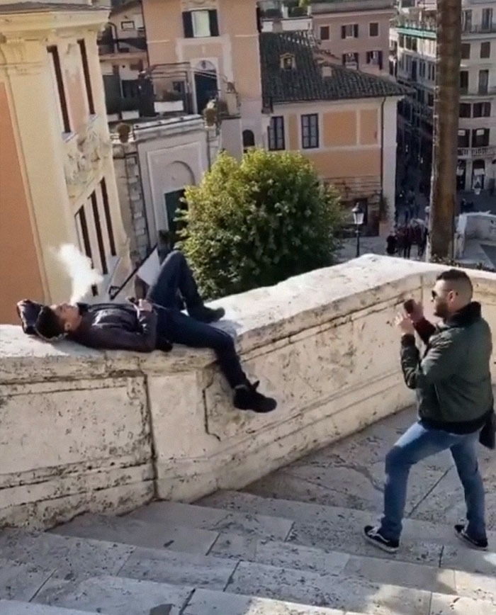 Man taking picture of laying man on railing