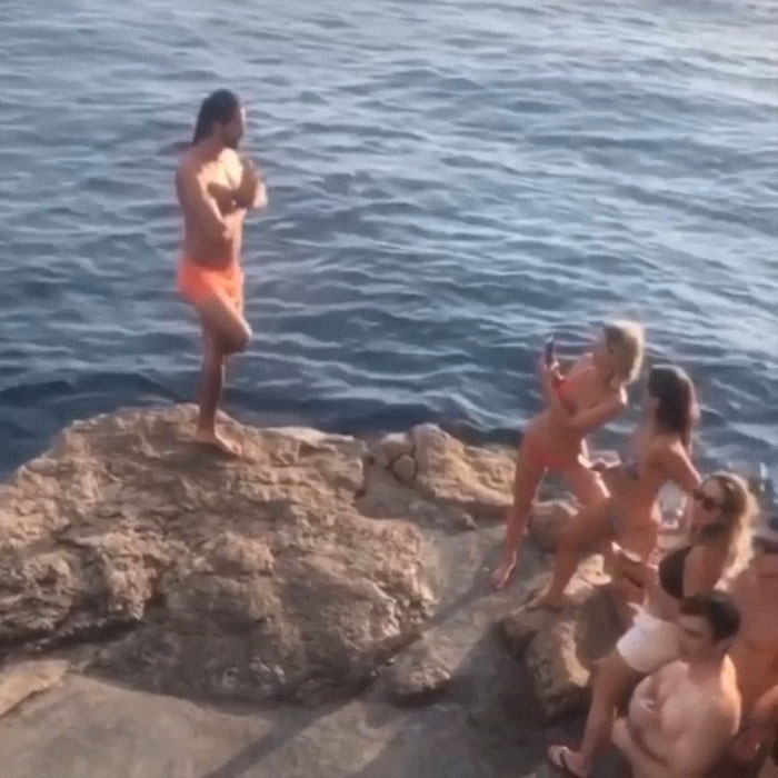 Woman taking a picture of a man posing on a rock above the sea 