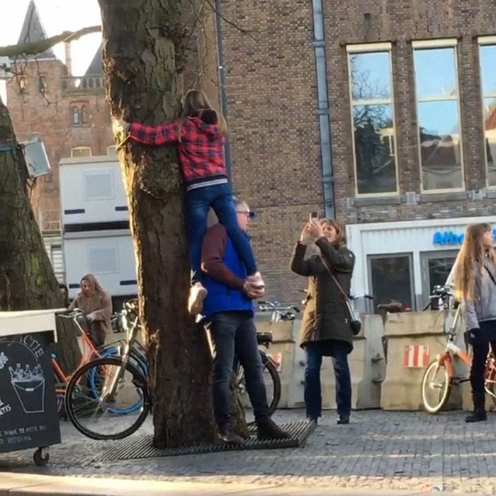Dad helping his girl to pose for a picture hugging the tree 