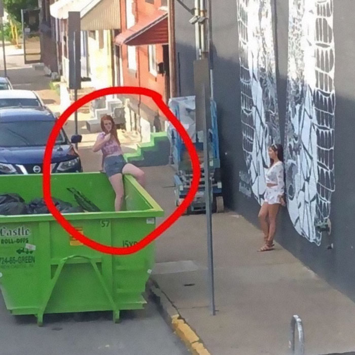 Girl posting in front of a wall while other girl is taking a picture white in trash can 