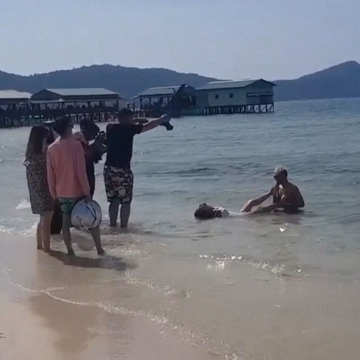 Man sucking toe of a woman in water while other people are taking pictures of them 