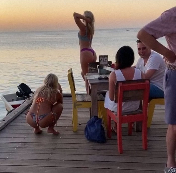 Girls posing on a bridge near water while people are eating 