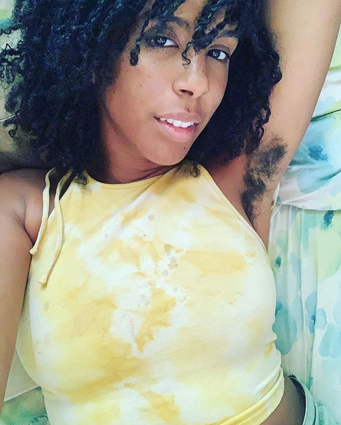 Woman with curly hair wearing a yellow tank top showing natural body hair as part of JanuHairy movement.