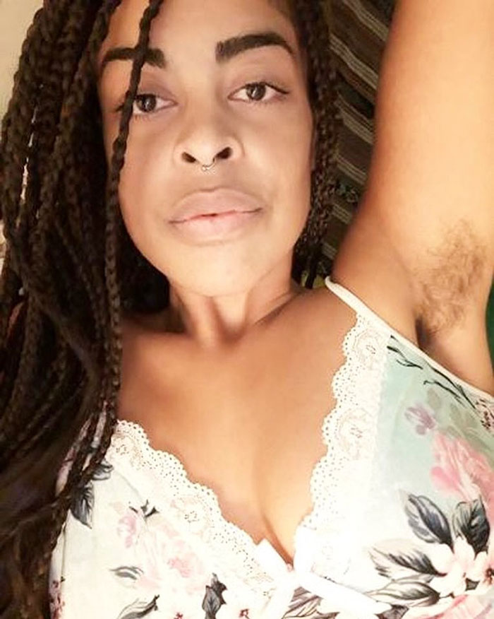 Woman showing natural hairy armpits and braided hair, embracing body positivity during JanuHairy campaign.