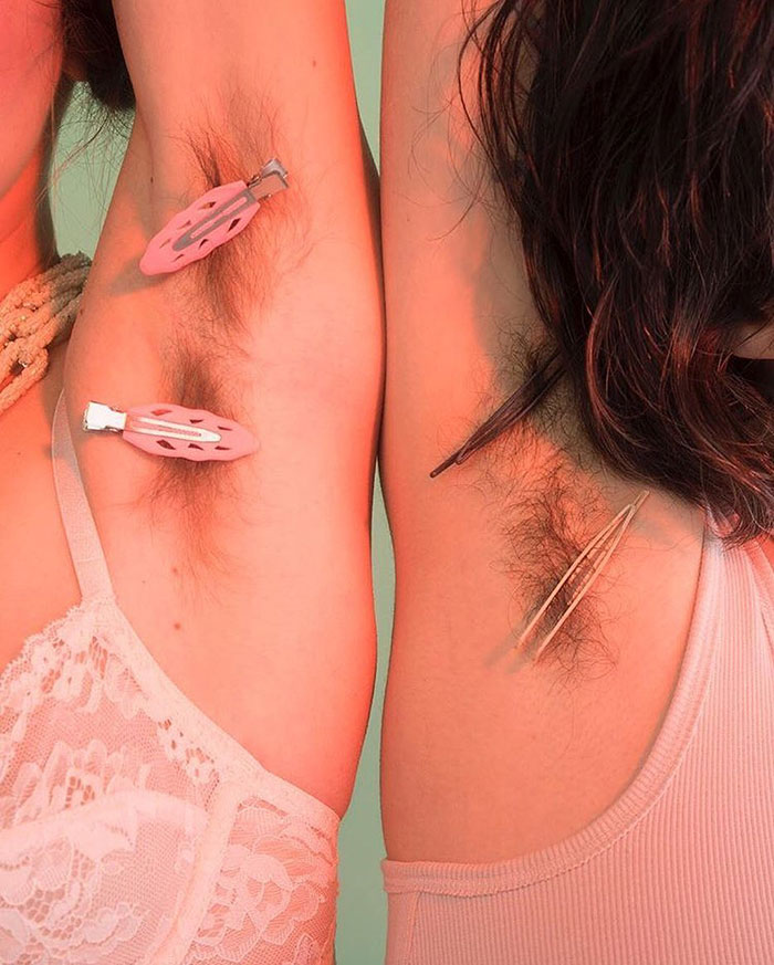 Two women showing natural armpit hair with clips, promoting body positivity during the JanuHairy campaign.