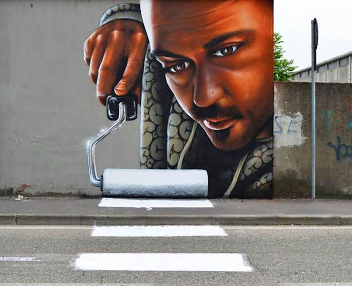 3D street art of a man painting a crosswalk on a wall, creatively interacting with the road and surroundings.