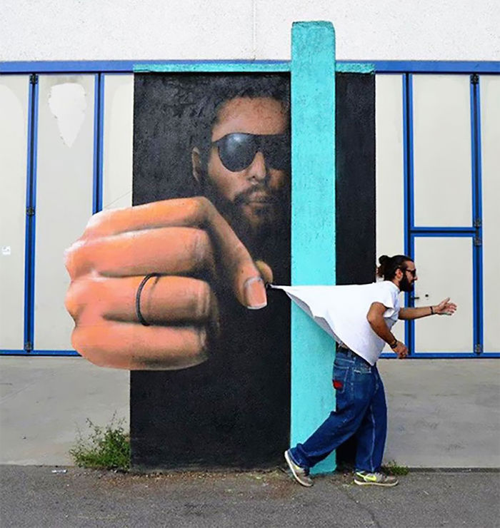 3D street art interacting with surroundings showing a man appearing to be pulled into a mural by a large painted hand.