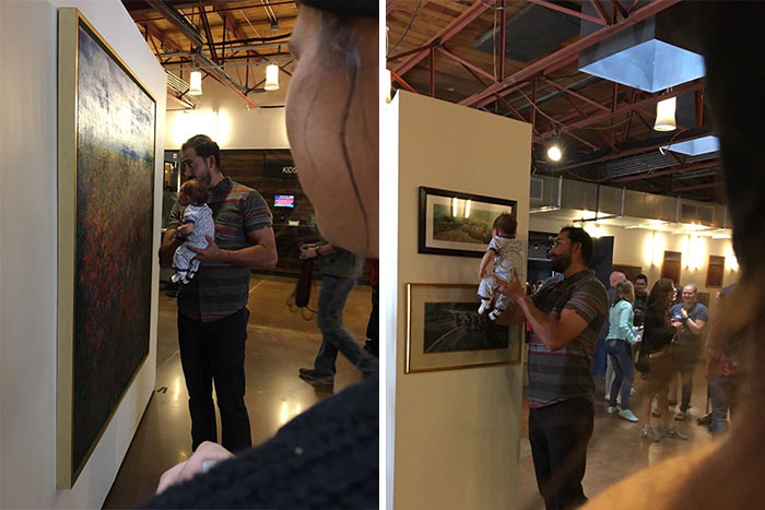 A Man Holding His Baby Up To Paintings And Talking To Him At An Art Gallery