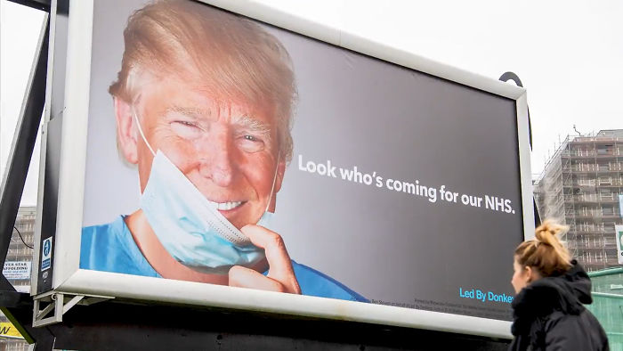 Billboard with a humorous Brexit meme, shows a person removing a mask, with text about NHS.