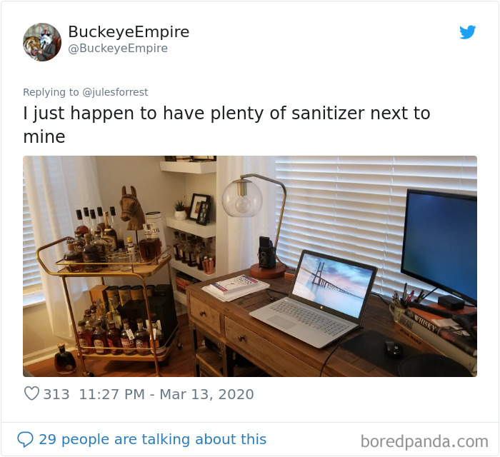 Home workspace setup with laptop, monitor, desk lamp, and a bar cart filled with liquor bottles, showing work from home reality.