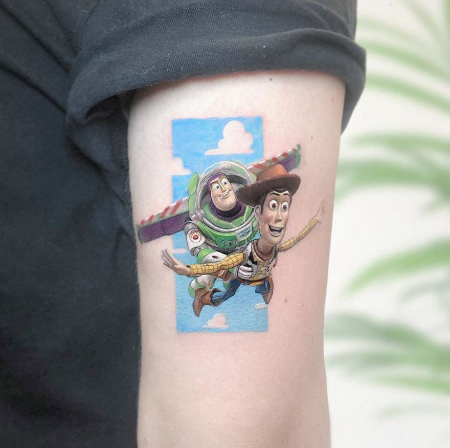 Colorful micro tattoo by Eden Kozokaro of two animated characters on an arm, resembling a pop culture painting.