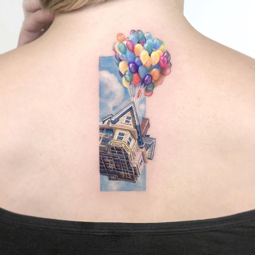 Colorful micro tattoo by Eden Kozokaro of a house with balloons on a person's upper back.