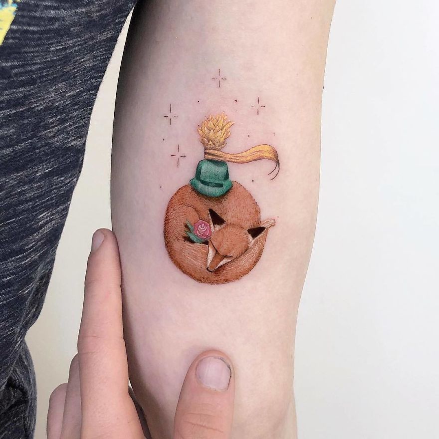 Colorful micro tattoo by Eden Kozokaro depicting a fox and person, resembling a mini pop culture painting on an arm.