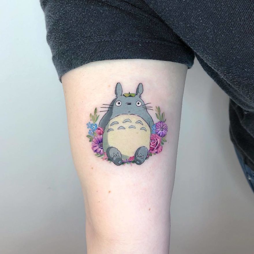 A colorful micro tattoo of a cute Totoro surrounded by flowers, showcasing pop culture art.