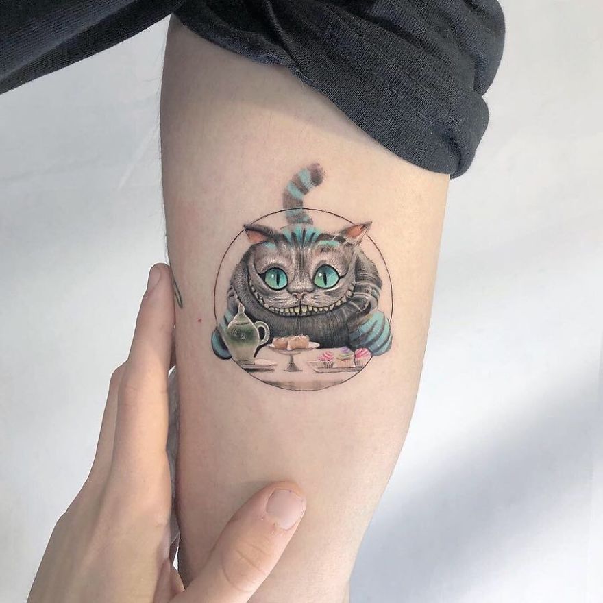 Colorful micro tattoo of a grinning cat by Eden Kozokaro, resembling a mini pop culture painting on an arm.