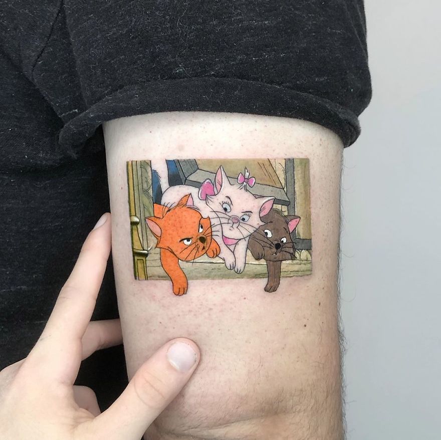Colorful micro tattoo by Eden Kozokaro of three animated cats on an arm, resembling a mini pop culture painting.