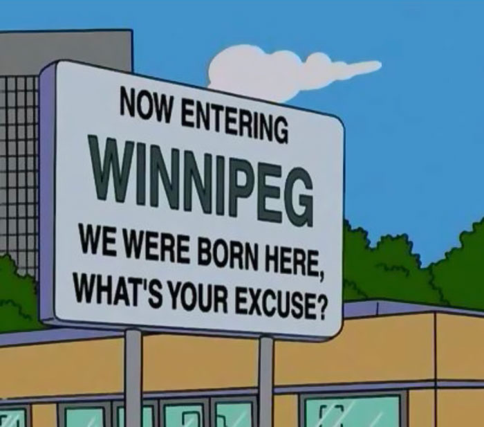Humorous Simpsons sign reading Now entering Winnipeg, we were born here, what's your excuse, highlighting witty signs.