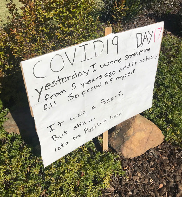 Sign with dad joke about fitting into old clothes during quarantine, posted in a garden setting.