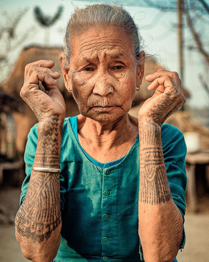 Senior woman with intricate tattoos on her arms, wearing a teal shirt, embodying how tattoos can look awesome at any age.