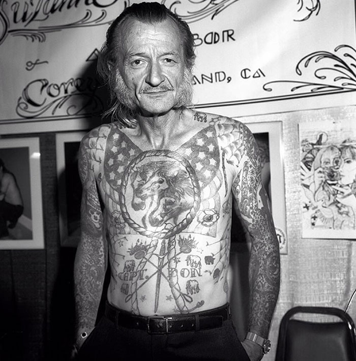 Senior man proudly displaying his detailed chest and arm tattoos at a tattoo convention.