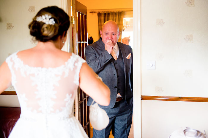 Emotional unstaged father-daughter moment as father sees bride in wedding dress for the first time indoors.