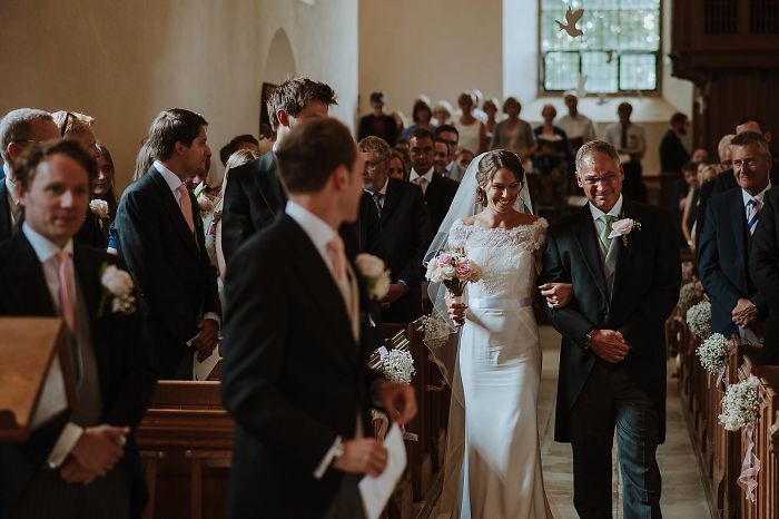 Bride and father walking down the aisle at a wedding, capturing an unstaged father-daughter moment.