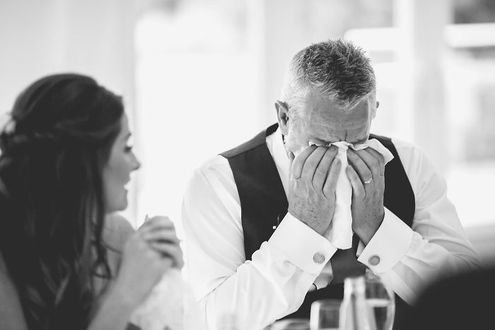 Emotional unstaged father-daughter moment at a wedding showing a father wiping tears while daughter looks on.