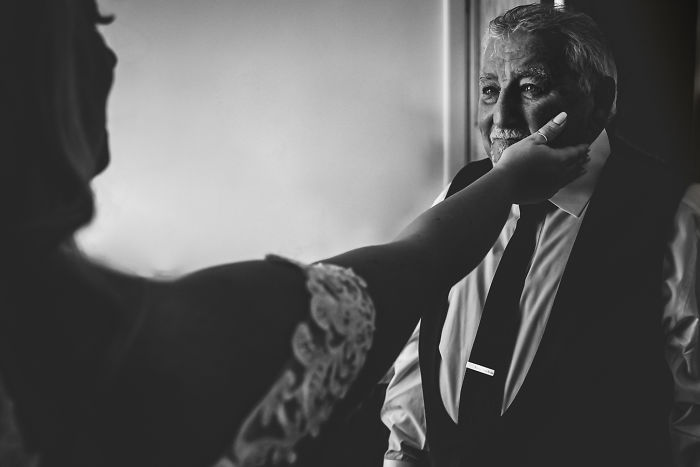 Unstaged father-daughter moment at wedding showing emotional connection with bride gently touching her father’s face.