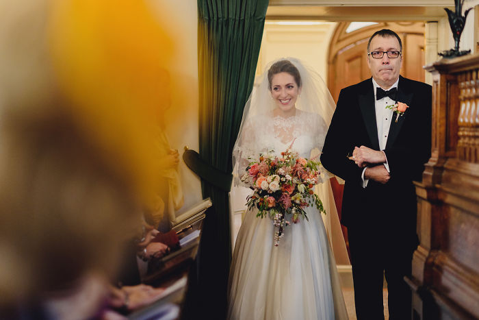 Bride smiling and holding a bouquet while walking down the aisle with her father in unstaged father-daughter moments at weddings
