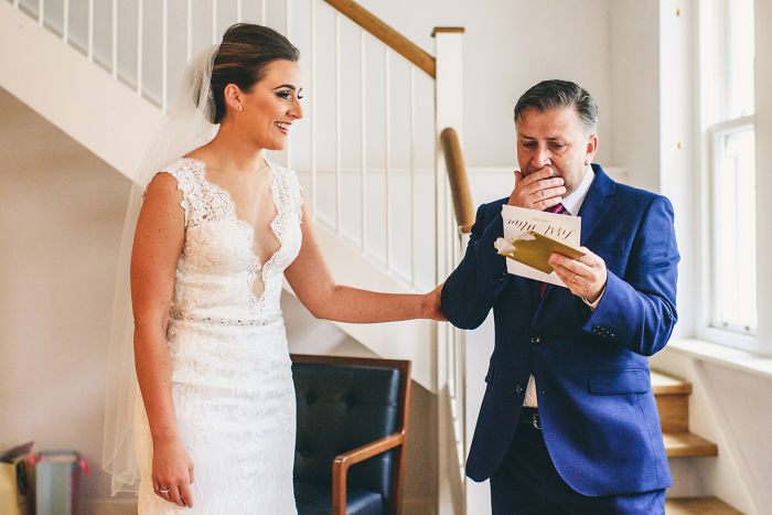 Bride in wedding dress sharing an unstaged father-daughter moment as he reads a heartfelt card before the ceremony.