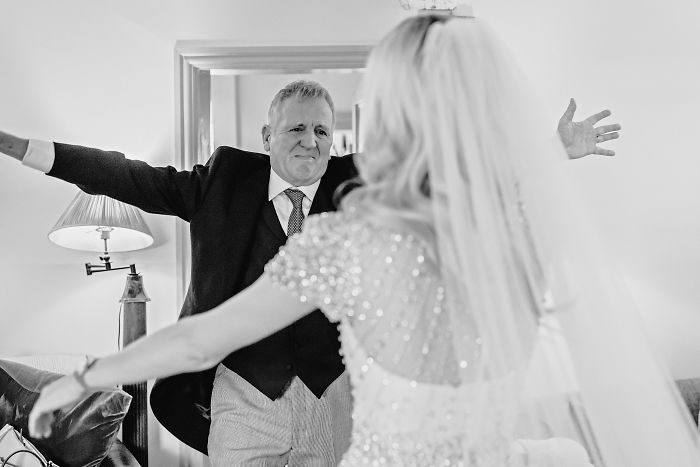 Father and daughter sharing an unstaged emotional moment at a wedding, arms open wide for a hug.