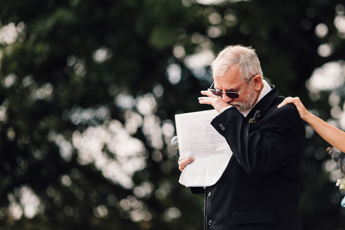 Emotional father-daughter moment at a wedding as the father wipes tears during an unstaged speech outdoors.