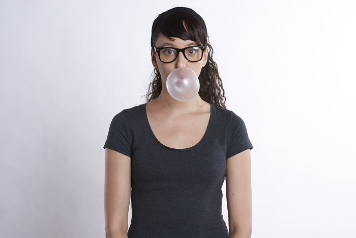 Young woman with glasses blowing a bubblegum bubble, illustrating employers rejecting job candidates during interviews.