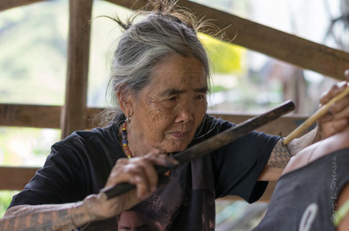 An elderly Filipino woman practicing ancient tattoo tradition with focused expression. An elderly Filipino woman practicing ancient tattoo tradition with focused expression.