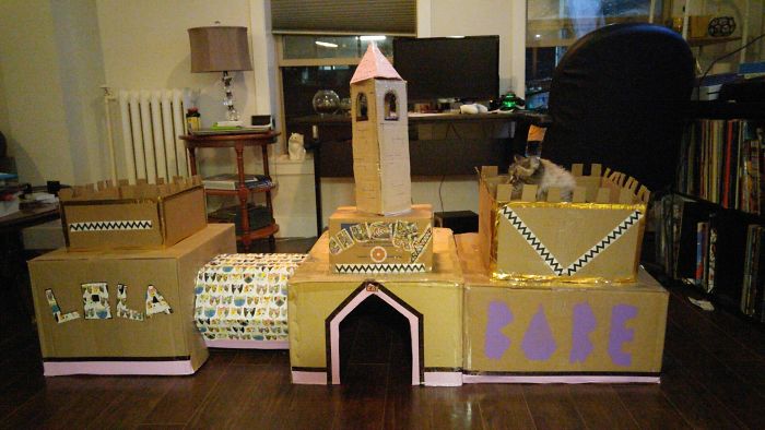 Cardboard fort for cats made from recycled boxes, featuring a tower and castle-like design in a living room setting.